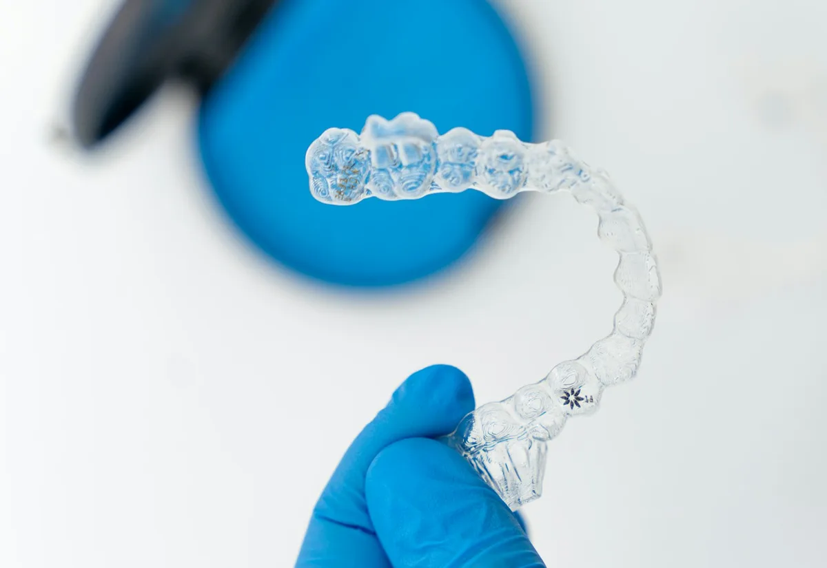 A clear aligner held in a gloved hand